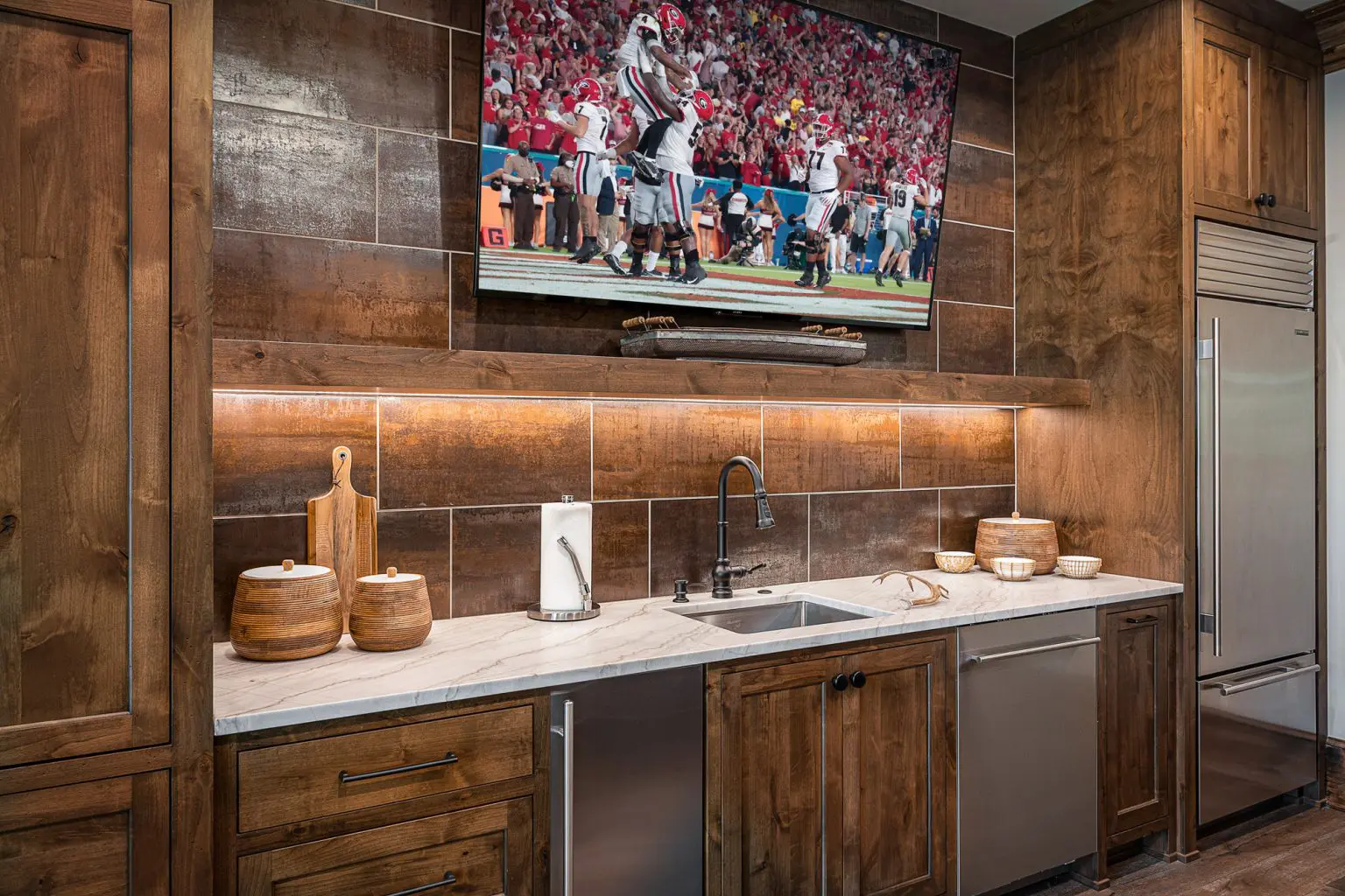 Elegant home bar with wood paneling and marble countertop, featuring a mounted TV, by Michael James Remodeling.